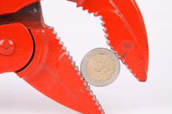 Ausschnitt einer roten Zange, die eine Zwei-Euro-Münze hält. 